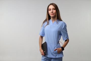 Confident female caucasian young nurse in blue scrubs with tablet