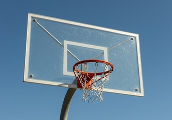 A clear acrylic basketball backboard mounted high above an outdoor court, featuring a vibrant orange rim and white nylon net ready for game play ,sport ,practice ,durable