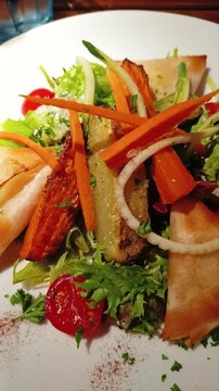 Assiette de samoussas croustillants accompagn&eacute;s d&rsquo;une salade fra&icirc;che avec tomates cerises, carottes, oignons et herbes, pr&eacute;sent&eacute;e sur une table de restaurant avec un dressage color&eacute; et app&eacute;tissant.