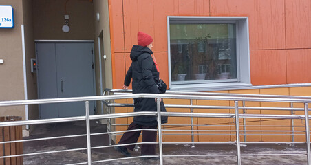 A woman walks down a ramp in winter wearing a red hat and coat.