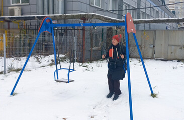 An adult woman swings on a blue swing on a snowy outdoor playground.