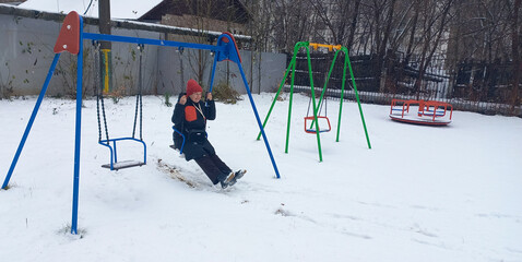 A happy 48-year-old woman swings on a swing at a snowy playground in winter.