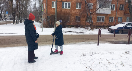 Woman talking to girl on scooter in snowy urban environment  