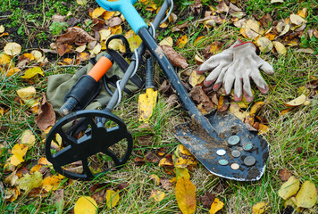 A person searches for buried coins in a park covered with colorful autumn leaves. Tools like a...