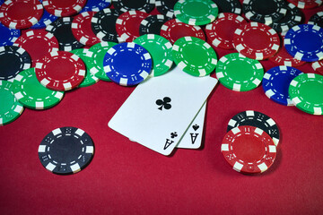 Players are engaged in a lively poker game featuring a mix of colored chips scattered across a red table along with two aces facing up, creating a thrilling atmosphere