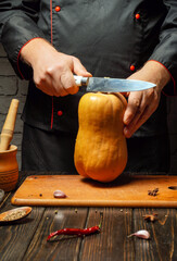 A chef is expertly cutting a fresh butternut squash on a wooden cutting board in a rustic kitchen. The atmosphere is warm with simple cooking utensils displayed