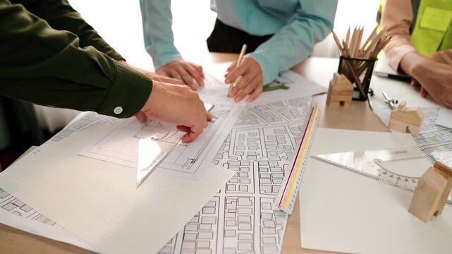 Smart architect and safety engineer discussion about building blueprint on table with architectural document, measurement tools and wooden block scatter around at modern office. Closeup. Delineation.