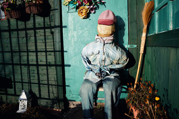 A scarecrow sitting on a wooden chair in front of a small garden gazebo on an allotment, cleverly imitating a resting human figure, basking peacefully in the warm sunlight of a golden autumn day.