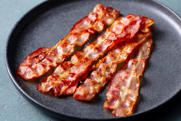 Crispy fried bacon on a black plate. Close up.