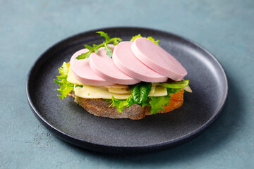 Delicious open sandwich with boiled sausage, cheese and fresh lettuce on rustic bread. Grey background. Close up.