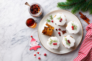 Festive Christmas puddings, cakes with white icing, rosemary and cranberries on a marble table. Copy space. Top view.
