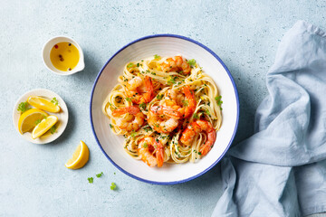 Fototapeta premium Delicious shrimp pasta dish with lemon accents and fresh herbs. Light blue background. Top view.