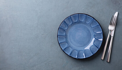 Empty blue plate with cutlery set. Grey background. Copy space. Top view.