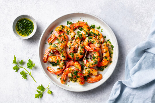 Grilled shrimps with chimichurri sauce on a white plate. Light grey background. Close up. Top view.