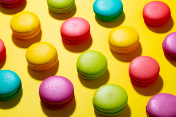 Vibrant macarons in rainbow hues arranged on sunny yellow backdrop. Flat lay composition. Close up.