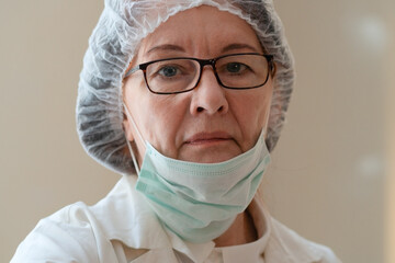 Close-up of a mature female doctor with her mask pulled down to the chin. Her tired eyes reflect exhaustion, dedication, and the human side of long-term health care work.