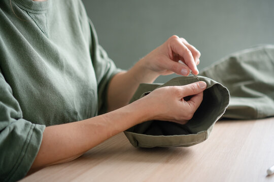 Female tailor using a seam ripper to carefully unpick the stitching on trousers. Close up of hands working in a sewing workshop.