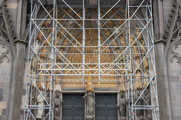 Architectural facade of a historic building under renovation, surrounded by scaffolding, showcasing intricate carvings and details, highlighting restoration efforts and craftsmanship in progress