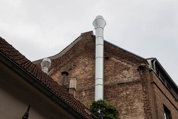Industrial building with brick facade featuring a tall metal chimney, surrounded by a cloudy sky, showcasing urban architecture and structural design elements