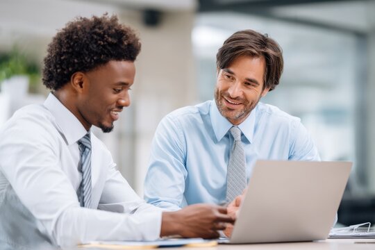 African American analyst and Caucasian businessman discussing data at a laptop in a meeting room. Perfect for teamwork and finance concepts.