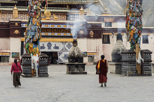 View of monks walking across the stone courtyard with prayer flags fluttering around incense burners in the ancient monastery, Shannan, Tibet, China.