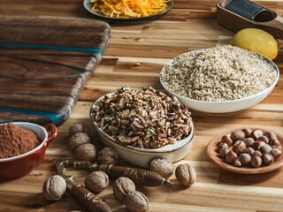 Chopped walnuts, cocoa powder, grated lemon zest, and various nuts are arranged on a rustic wooden table, highlighting the essential ingredients for cozonac baking