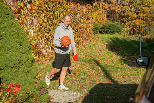 osoba w stroju sportowym idąca z piłką do koszyk&oacute;wki oraz rakietkami do ping ponga