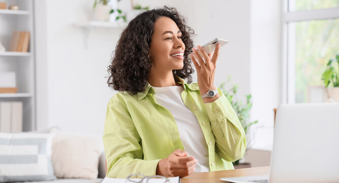 Young African-American woman using mobile phone for searching online at workplace