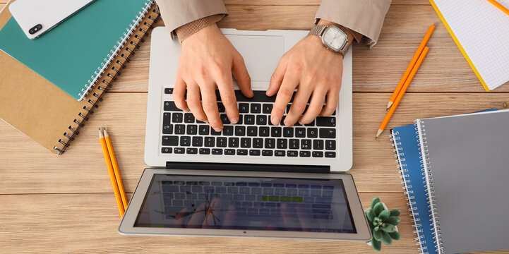 Hands of businessman using laptop at wooden table, top view