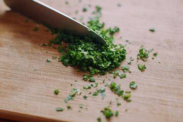 Close up overhead shot of a chef s knife finely chopping fresh green herbs on a wooden cutting board for culinary preparation