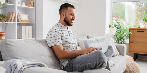 Young man using laptop while sitting on sofa at home