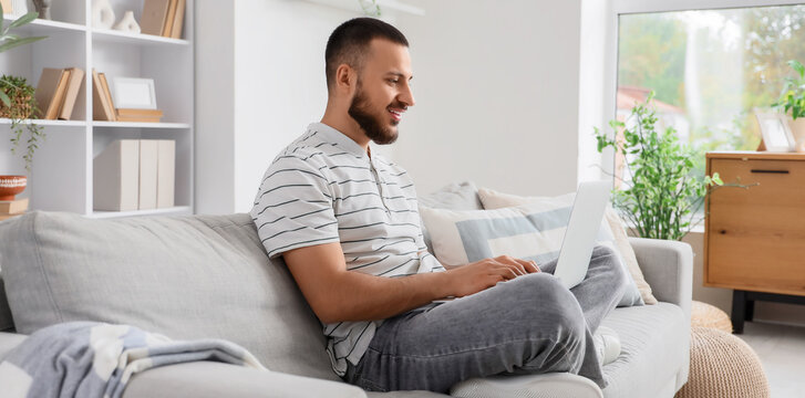 Young man using laptop while sitting on sofa at home - Powered by Adobe