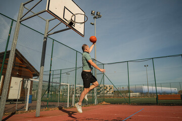 osoba rzuca, bawi się piłką do koszykówki na boisku na zewnątrz w słoneczny dzień © siwyk
