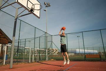 osoba rzuca, bawi się piłką do koszykówki na boisku na zewnątrz w słoneczny dzień © siwyk