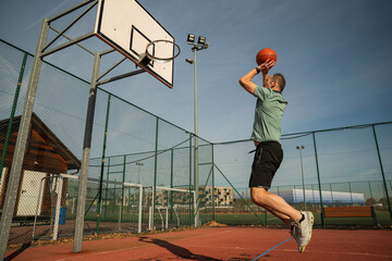 osoba rzuca, bawi się piłką do koszykówki na boisku na zewnątrz w słoneczny dzień © siwyk