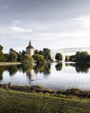 View of a tranquil lake reflecting the soft light of the sky and the medieval castle tower surrounded by lush greenery, Malmo, Skane County, Sweden.
