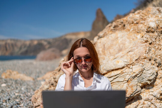 Digital nomad woman working on laptop at sunny beach, enjoying remote work vacation lifestyle