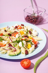 Plate of tasty pasta salad with tomatoes and beans on lilac background