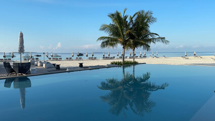Luxury resort photo of Maldives tropical paradise island in Indian Ocean with swimming pool, palm trees, beach umbrella and chair. Beautiful photography, azure ocean, sky with clouds.