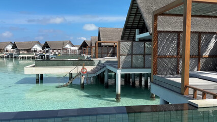 Luxury resort photo of Maldives tropical paradise island in Indian Ocean with overwater thatched bungalows, swimming pool. Beautiful photography, coral reef, azure ocean, sky with clouds. 
