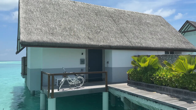 Luxury resort photo of Maldives tropical paradise island in Indian Ocean with palm trees, overwater thatched bungalows, bicycle. Beautiful photography, coral reef, azure ocean, sky with clouds.  - Powered by Adobe