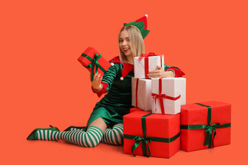 Young woman in elf costume with Christmas gift boxes on orange background