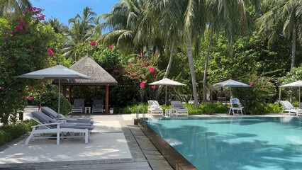 Luxury resort photo of Maldives tropical paradise island in Indian Ocean with swimming pool, palm trees, beach umbrella, chair. Beautiful photography, wooden house, sky with clouds.