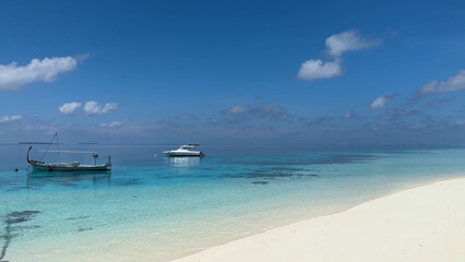 Luxury resort photo of Maldives tropical paradise island in Indian Ocean with yacht or boat on water. Beautiful photography, coral reef, azure ocean, 
sky with clouds on horizon. 