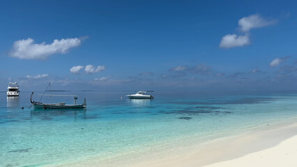 Luxury resort photo of Maldives tropical paradise island in Indian Ocean with yacht or boat on water. Beautiful photography, coral reef, azure ocean, 
sky with clouds on horizon. 