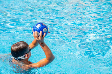 young athletic boy playing ball in the pool