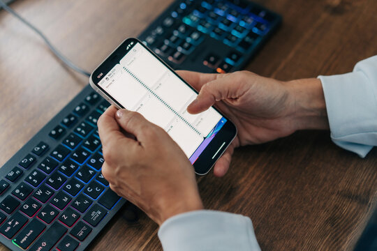 Close-up  hands using a mobile phone at a desk in the workplace typing plans in an electronic organizer. - Powered by Adobe