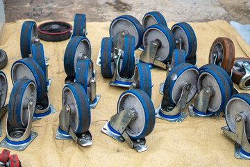 Metal and rubber transport caster wheels with blue rims displayed at a tool market, components for carts and industrial equipment.