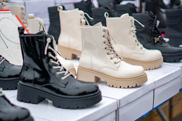 Beige and black women’s ankle boots with chunky heels displayed on boxes at a shoe market, autumn fashion, leather footwear.