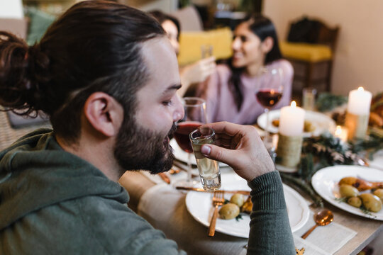 young latin man and group of friends toasting with tequila shots for christmas dinner or thanksgiving in Mexico Latin America, hispanic people at holidays - Powered by Adobe